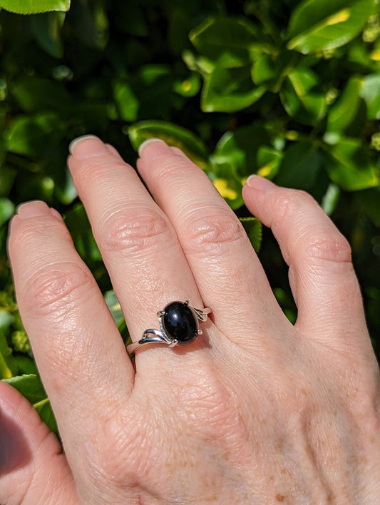 Hand wearing a silver ring with a black gemstone against a green leafy background