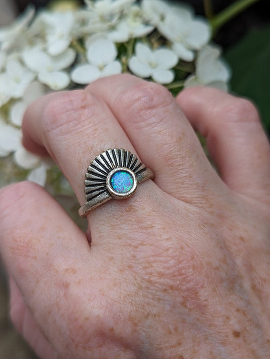 Hand wearing an Art Deco Fan Ring with Iridescent Blue Opal - Silver Finish against a white flower background