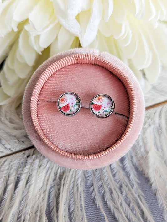 Pair of dainty 8mm pink rose stud earrings in stainless steel settings in a pink jewelry box with white flowers in the background