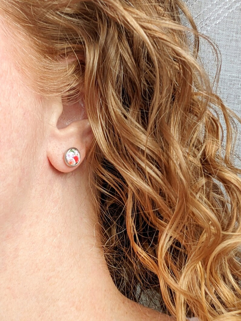 Close-up of a model wearing a pair of dainty 8mm pink rose stud earrings in stainless steel settings.