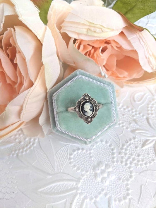Greek Goddess Shield Cameo Ring - Antiqued Silver Brass Signet with an ivory on black cameo in a hexagonal box with pink flowers on a textured white surface.