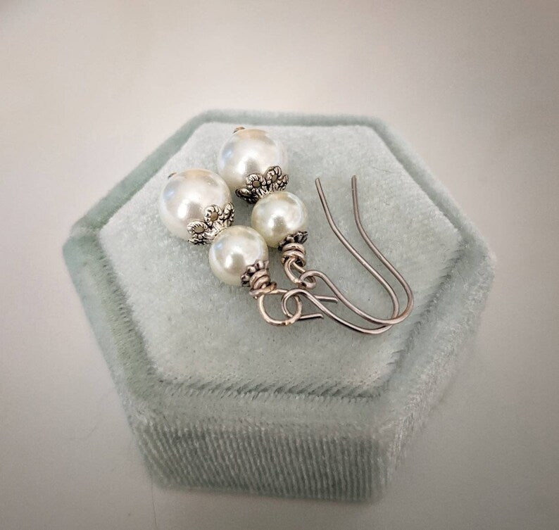 Pair of ivory double pearl drop earrings with antiqued silver filigree bead caps,on a hexagonal green velvet stand