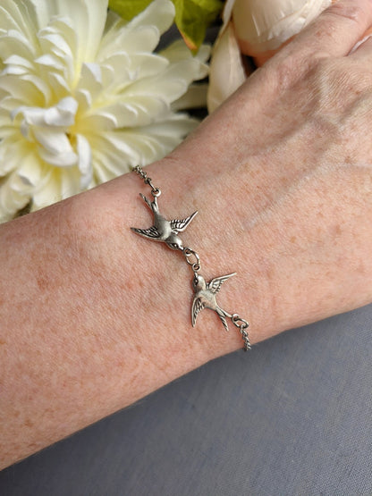 Silver Swallow two Bird Bracelet with toggle clasp- minimalist nature  jewelry on a wrist with a white flower in the background