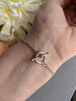 Silver bracelet with a toggle clasp on a wrist, with a blurred background of flowers.