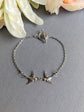 Silver Swallow two Bird Bracelet with toggle clasp- minimalist nature  jewelry on a gray surface with flowers in the background