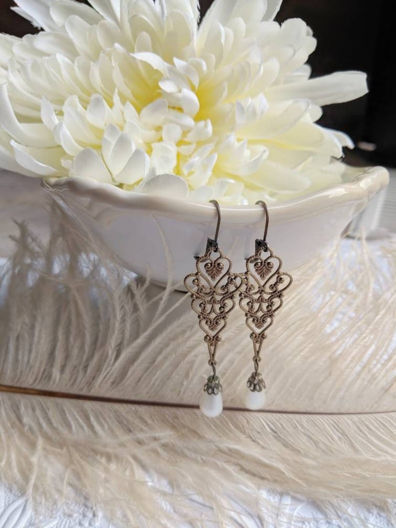 Long Victorian Pearl Drop Earrings - Bronze Filigree Bridal Dangles on a white feathered surface with a white flower in the background