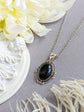 Black Obsidian Crystal Necklace - Silver Flourish Pendant Setting on a gray surface with flowers and decorative elements.