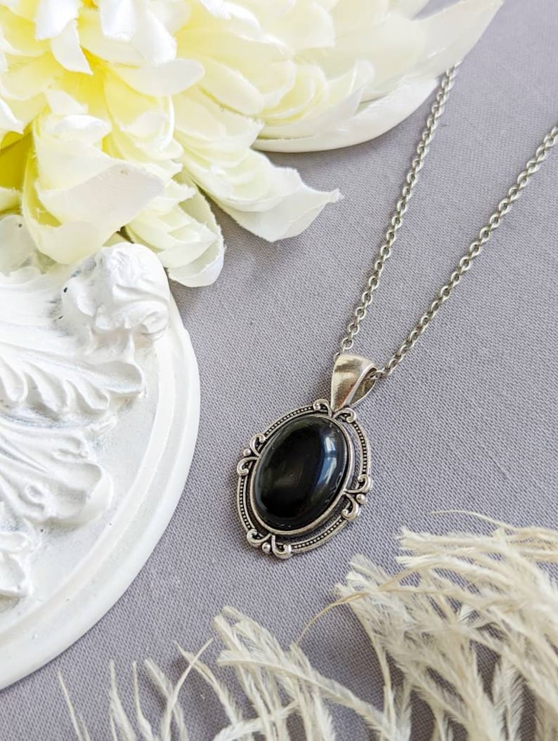 Black Obsidian Crystal Necklace - Silver Flourish Pendant Setting on a gray surface with flowers and decorative elements.