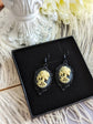 Pair of gothic black skull cameo drop earrings with detailed ivory lolita skull reliefs on a black display box with a decorative white background.