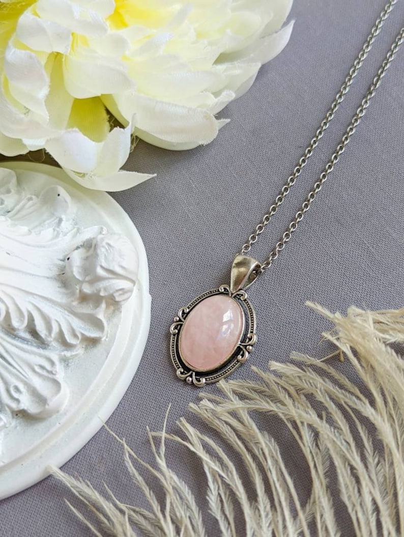 Pale Pink Rose Quartz Crystal Necklace - Silver Flourish Pendant Setting on a gray surface with flowers and feathers
