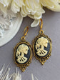 Pair of gothic black skull cameo drop earrings with detailed ivory lolita skull reliefs on a gray surface with white flowers.