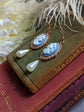 Side view of blue cameo pearl drop earrings in lacy 14k rose gold plated settings on a book