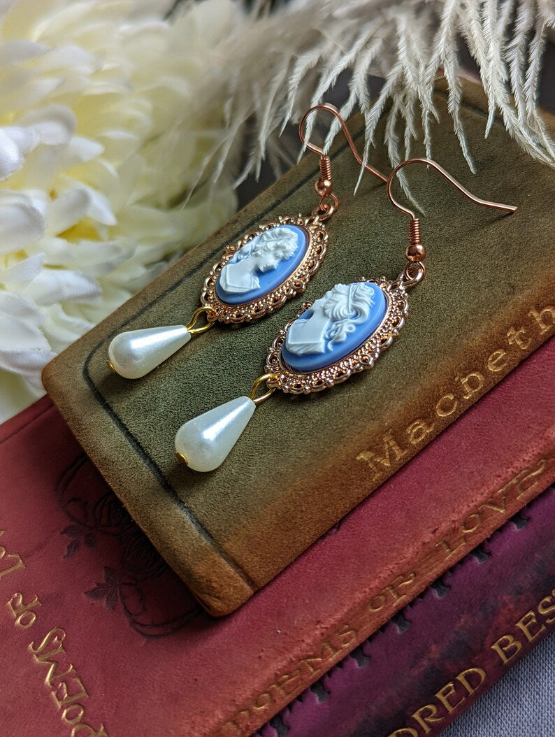 Side view of blue cameo pearl drop earrings in lacy 14k rose gold plated settings on a book
