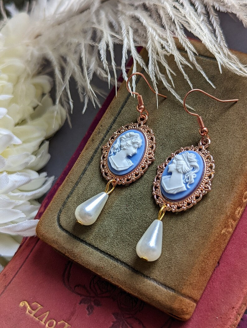 Blue cameo pearl drop earrings in lacy 14k rose gold plated settings on a book