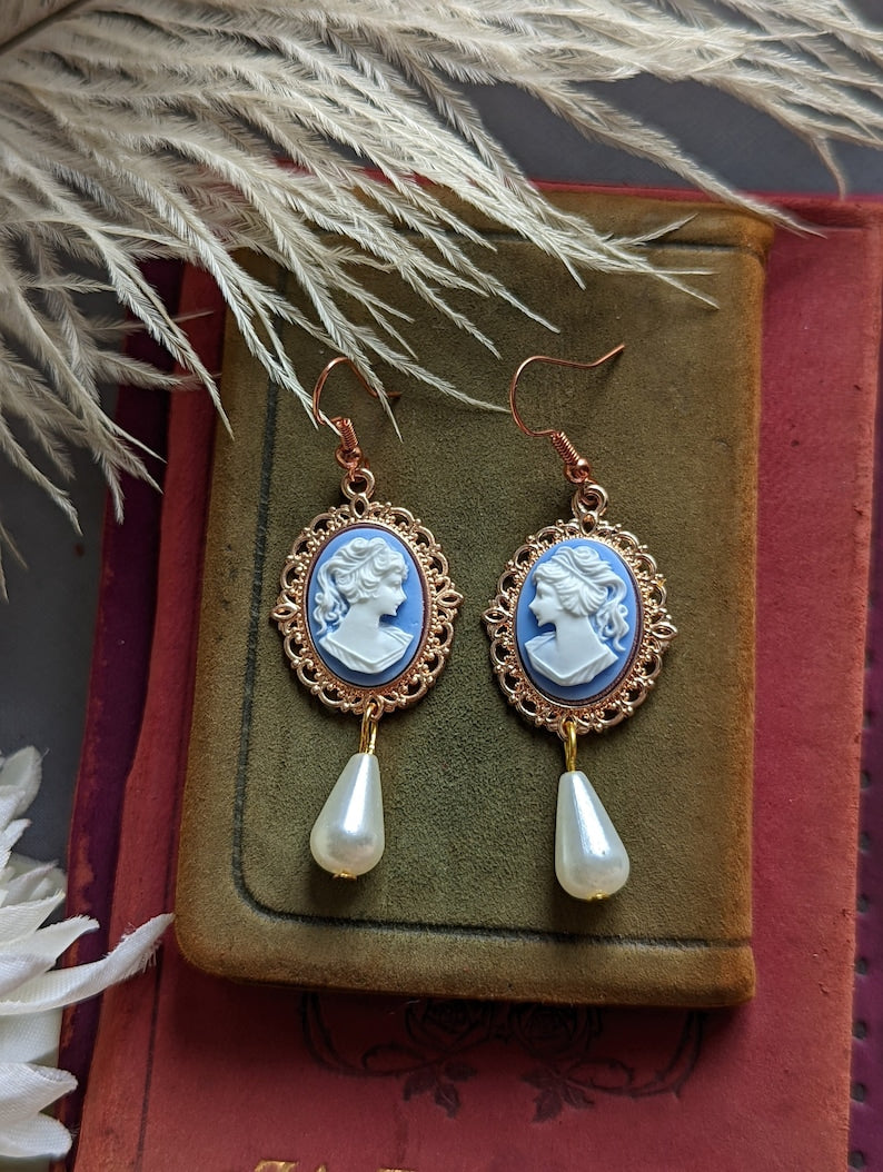 Blue cameo pearl drop earrings in lacy 14k rose gold plated settings on a textured surface.