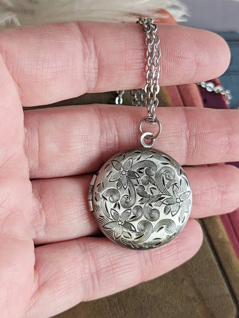 Silver round floral etched locket necklace by Papillion Era held in a hand