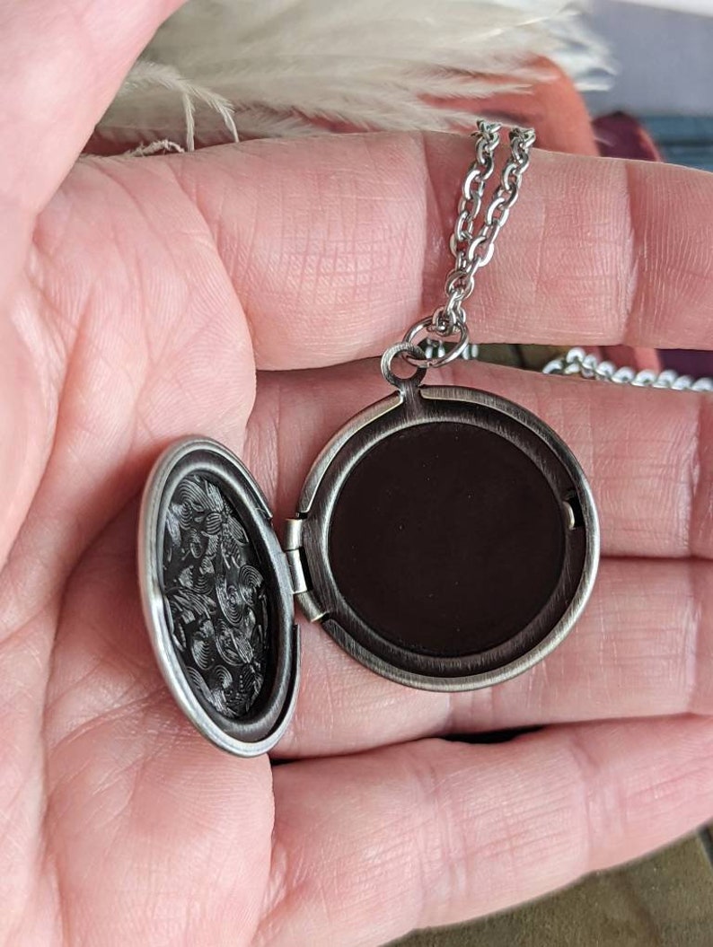 Open Silver round floral etched locket necklace by Papillion Era held in a hand