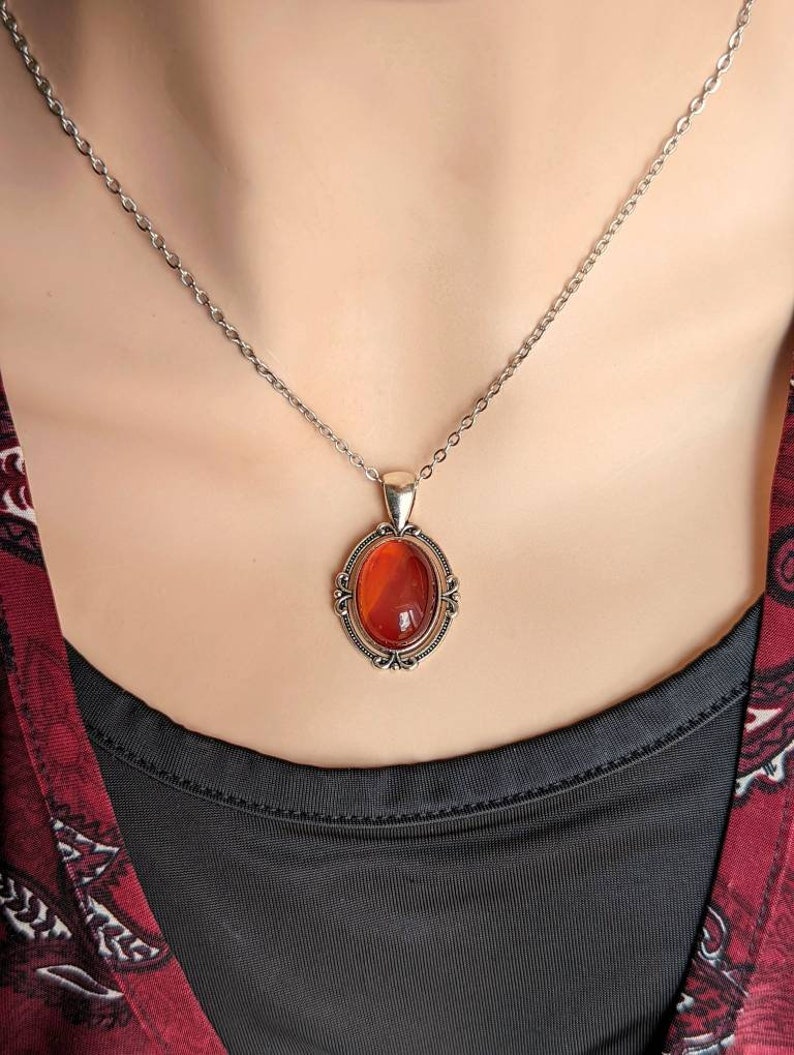 Red Carnelian Crystal Necklace - Silver Flourish Pendant Setting worn by a person, with a blurred background.