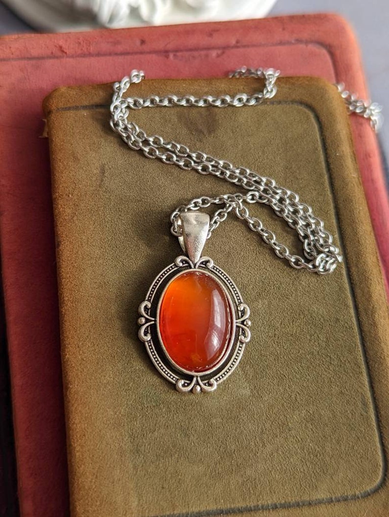 Red Carnelian Crystal Necklace - Silver Flourish Pendant Setting on a brown velvet surface