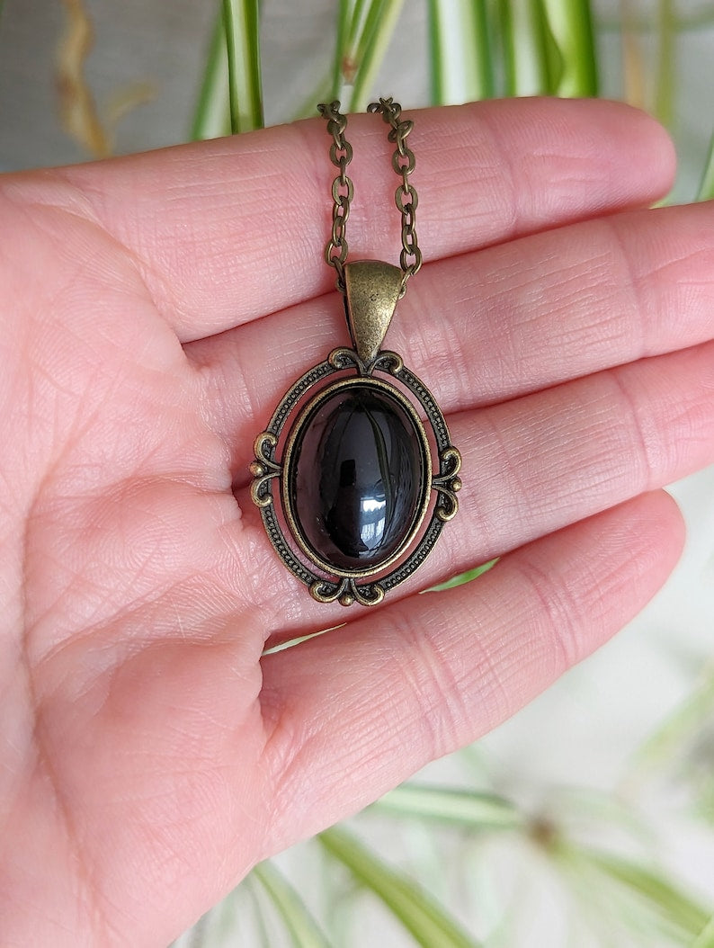 Black Obsidian Crystal Necklace - Bronze Flourish Pendant Setting held in a hand against a blurred natural background