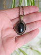 Black Obsidian Crystal Necklace - Bronze Flourish Pendant Setting held in a hand against a blurred natural background