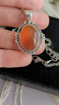Red Carnelian Crystal Necklace - Silver Flourish Pendant Setting held in a hand against a neutral background