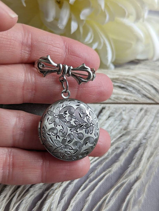 Silver round floral etched locket brooch pin by Papillion Era being held