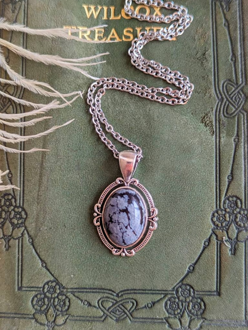 Snowflake Obsidian Crystal Necklace - Silver Flourish Pendant Setting on a green vintage book.