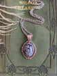 Snowflake Obsidian Crystal Necklace - Silver Flourish Pendant Setting on a green vintage book.