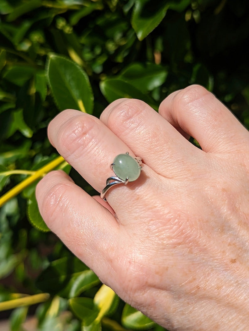 Hand wearing a Natural Green Aventurine Solitaire Ring - Sterling Silver - Handmade Gemstone Jewelry - Made in Toronto against a green leafy background