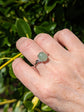 Hand wearing a Natural Green Aventurine Solitaire Ring - Sterling Silver - Handmade Gemstone Jewelry - Made in Toronto against a green leafy background