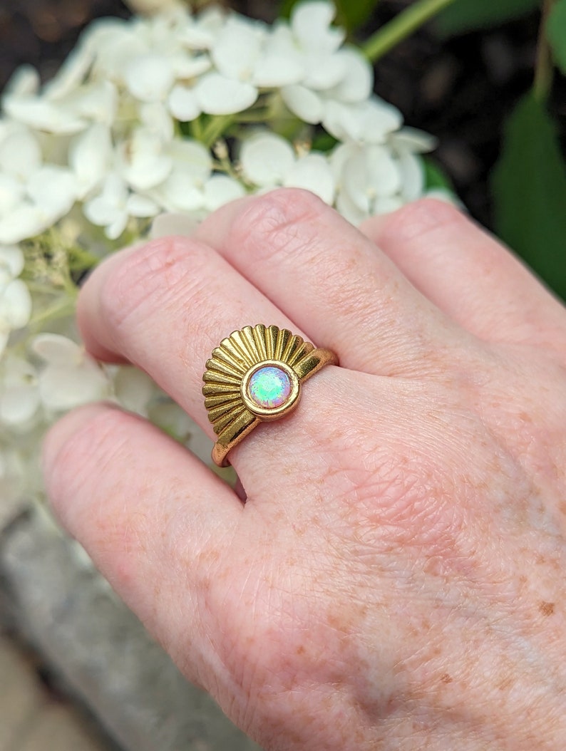 Art Deco Fan Ring with Iridescent Pink Opal - Gold Finish on a hand, with white flowers in the background