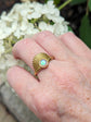 Art Deco Fan Ring with Iridescent Pink Opal - Gold Finish on a hand, with white flowers in the background