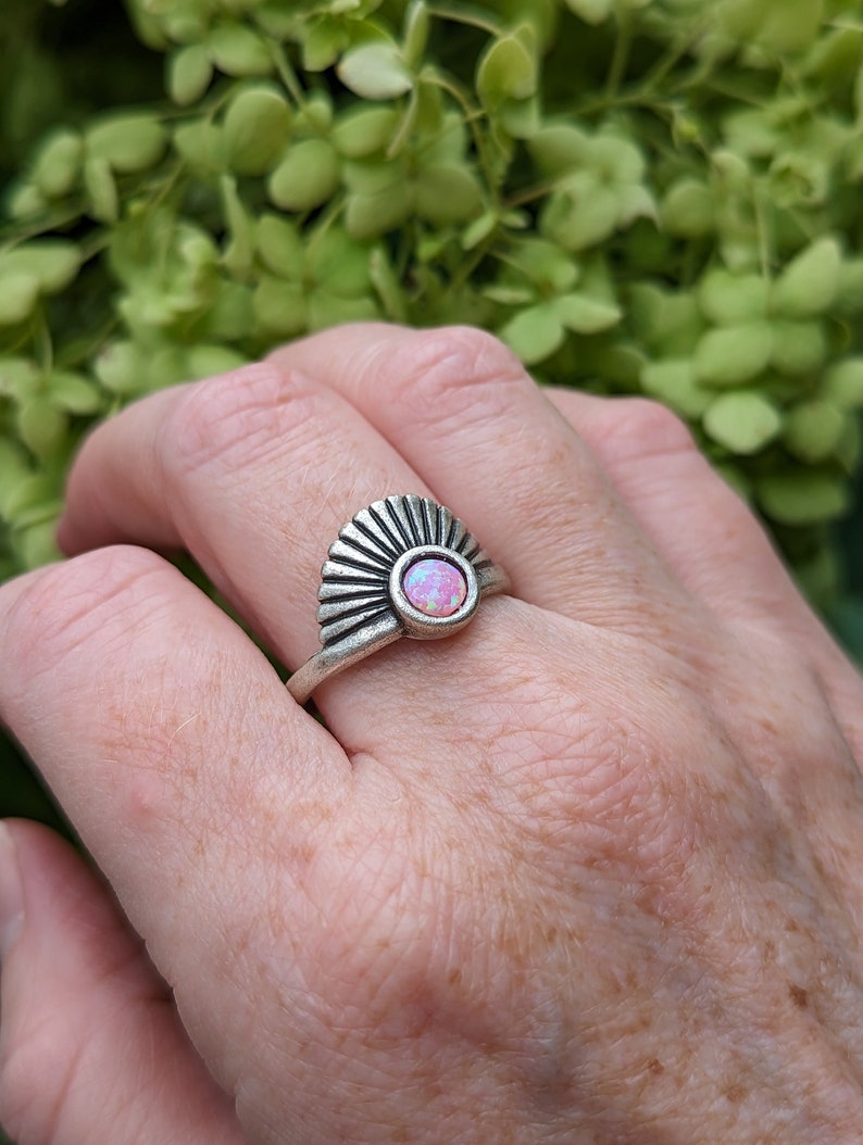 Art Deco Fan Ring with Iridescent Pink Opal - Silver Finish on a person's finger against a green leafy background