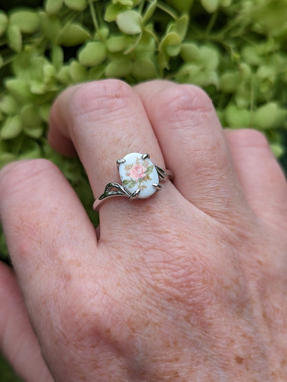 Pink Rose Cameo Ring - Sterling Silver Adjustable Band on a person's finger against a green leafy background