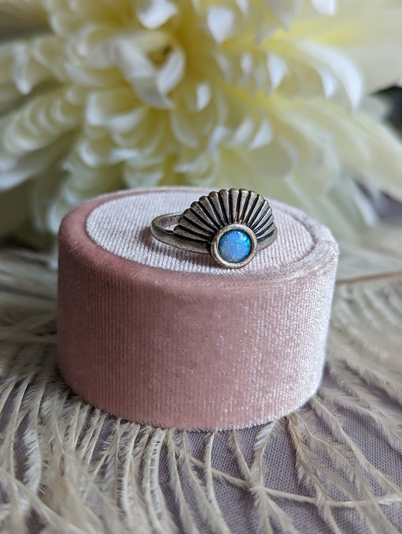 Art Deco Fan Ring with Iridescent Blue Opal - Silver Finish on a pink velvet cushion, with white flowers in the background
