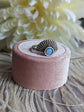 Art Deco Fan Ring with Iridescent Blue Opal - Silver Finish on a pink velvet cushion, with white flowers in the background