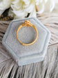 Side view of matte gold ring in a hexagonal light blue velvet box on a fluffy white surface with flowers in the background.