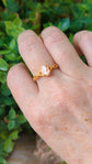 Matte gold cameo ring with single loop shoulder detail on a hand against a green leafy background.