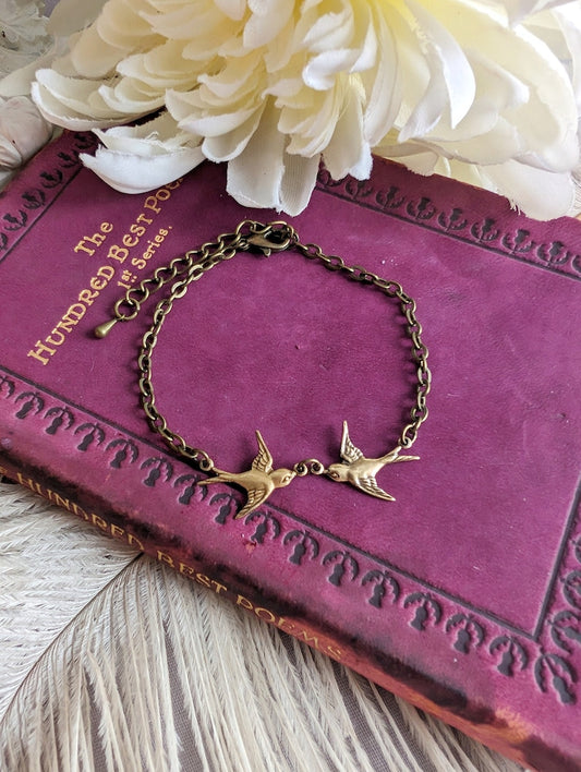 Dainty Swallow Bracelet: Antiqued Brass Bird Charm, Minimalist Jewelry on a purple book