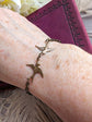 Dainty Swallow Bracelet: Antiqued Brass Bird Charm, Minimalist Jewelry on a wrist, with a purple book and flowers in the background