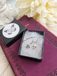Fleur de Lis Earrings - Pewter French Lily Flower - Victorian Jewelry in a jewelry box with a brand logo on a decorative surface.
