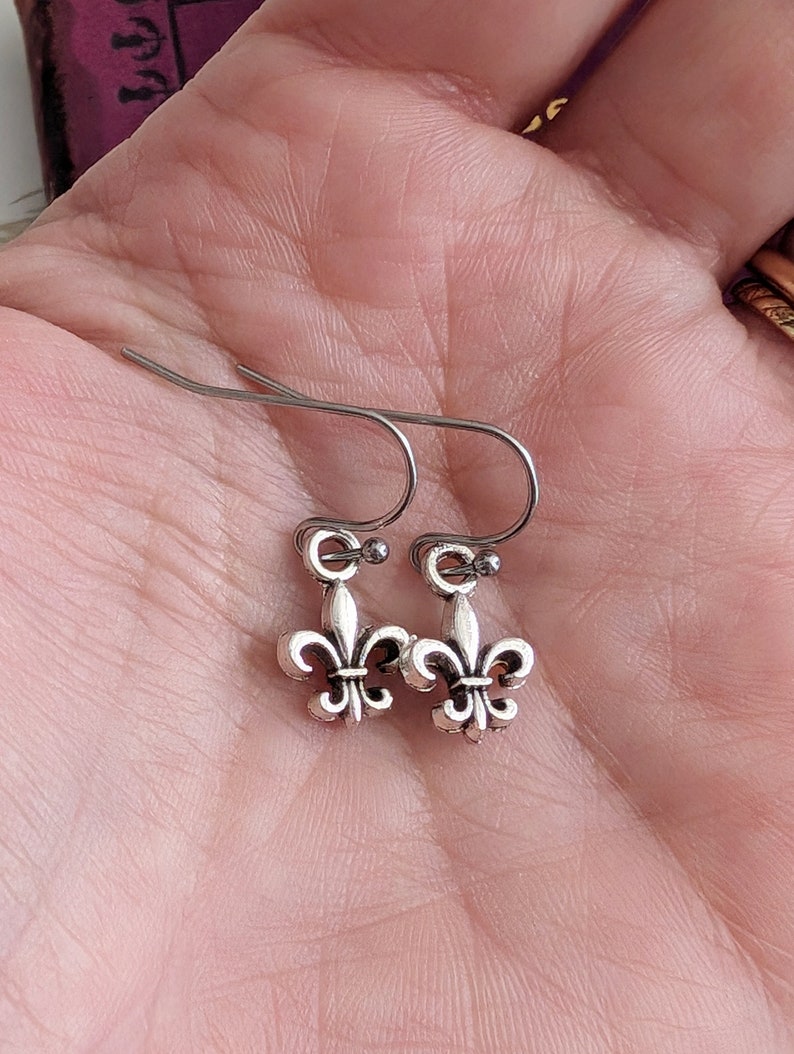 Silver fleur-de-lis earrings held in a hand