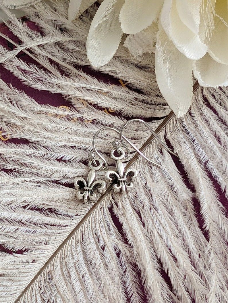Fleur de Lis Earrings - Pewter French Lily Flower - Victorian Jewelry on a feather with white flowers in the background