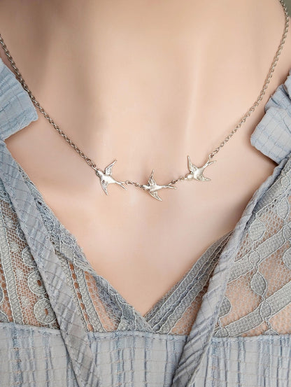Antiqued silver vintage-style necklace with three flying bird pendants on a person wearing a light blue lace blouse.