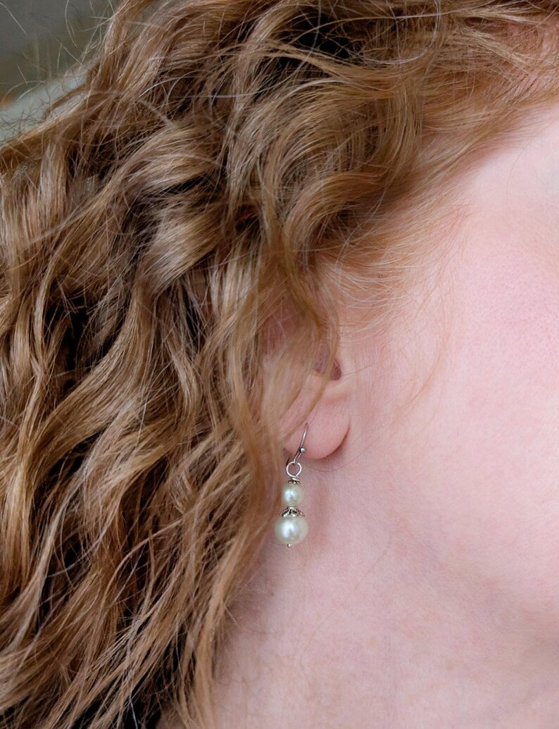 Close-up of an ear with an ivory double pearl drop earring with antiqued silver filigree bead cap.