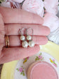 Close up of a pair of ivory double pearl drop earrings with antiqued silver filigree bead caps, being held.