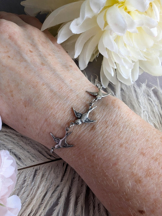 Silver Swallow Bird Bracelet: Dainty Trio Jewelry, Minimalist Style on a wrist, with white flowers in the background