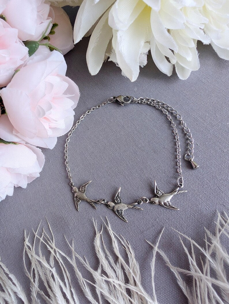 Silver Swallow Bird Bracelet on a gray surface with pink and white flowers and dried grasses.