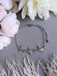 Silver Swallow Bird Bracelet on a gray surface with pink and white flowers and dried grasses.
